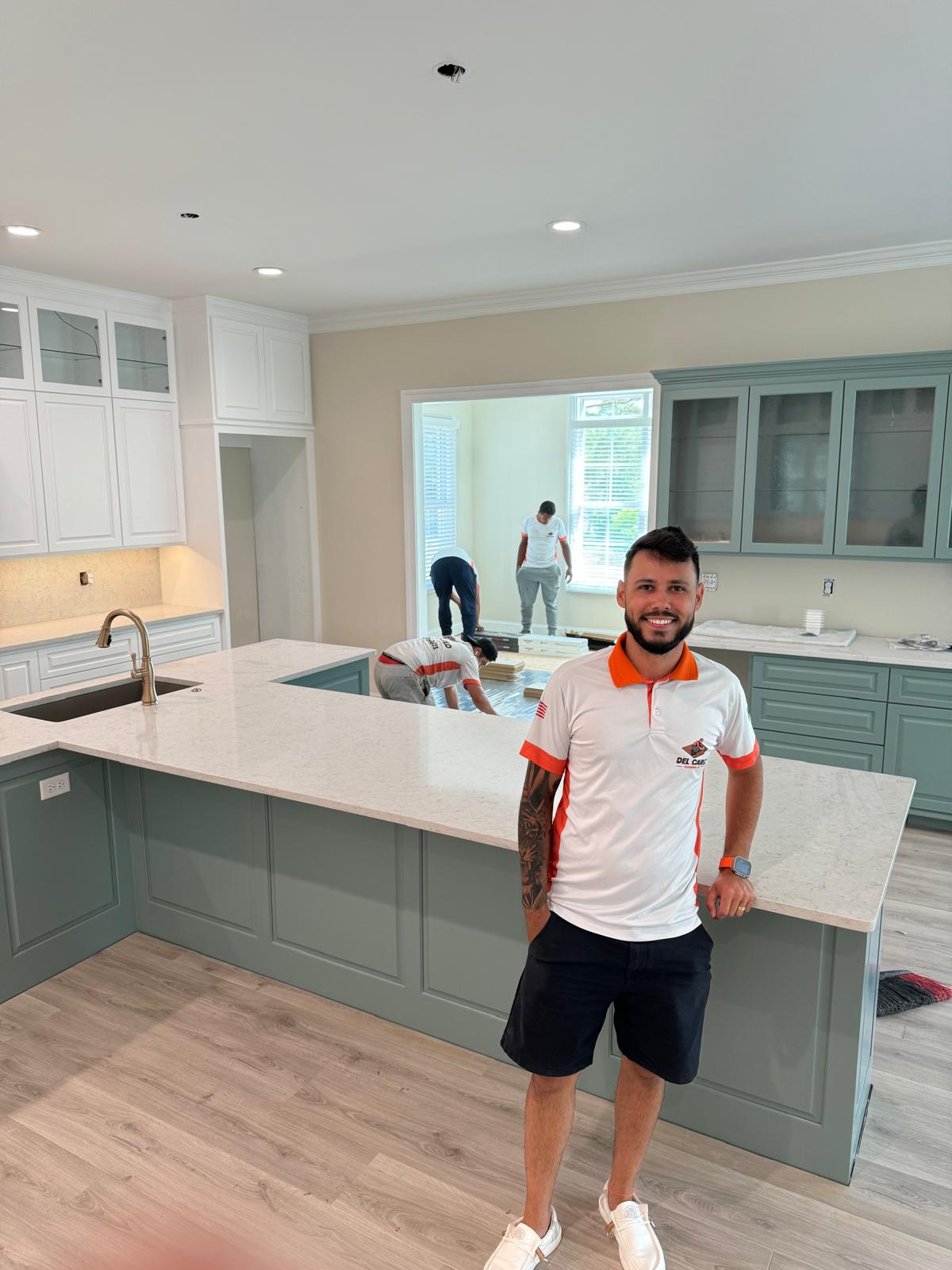 Fúlvio Del Carlo standing in a remodeled kitchen with the Del Carlo Flooring crew installing flooring in the background